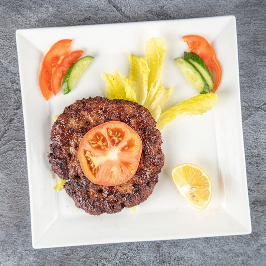 A plate of ChicnBe's deliciously crispy and juicy Beef Chapli Kababs, golden-brown and perfectly cooked, garnished with fresh herbs, onions, and lime wedges, offering an authentic taste of traditional flavors.