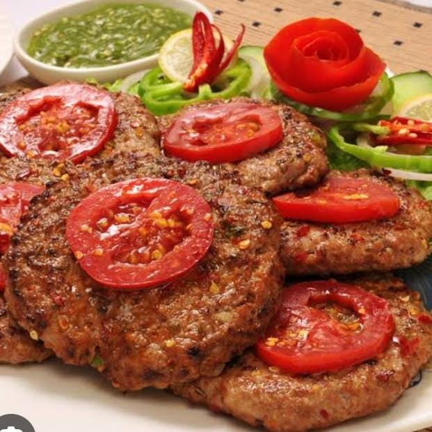 A plate of ChicnBe's deliciously crispy and juicy Beef Chapli Kababs, golden-brown and perfectly cooked, garnished with fresh herbs, onions, and lime wedges, offering an authentic taste of traditional flavors.
